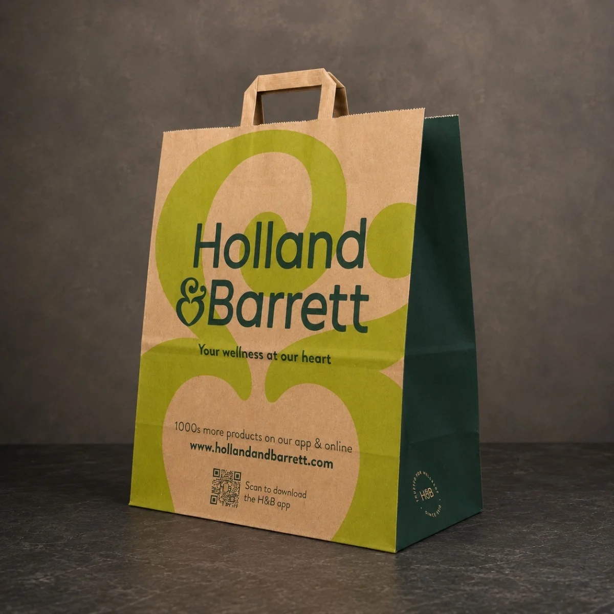 Brown And Green Holland & Barrett Printed Kraft Paper Bag With Natural Flat Handles On A Dark Stone Surface